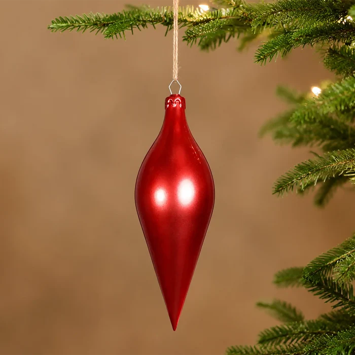 A glossy red finial Christmas ornament hanging from a tree branch against a warm brown background.