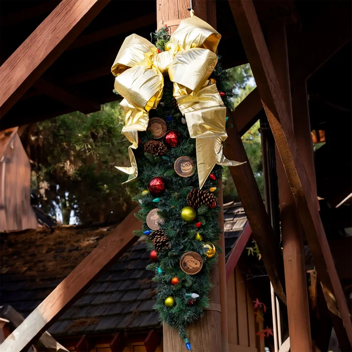 Decorative Christmas wreath with gold bows and colorful ornaments hanging on a wooden structure.