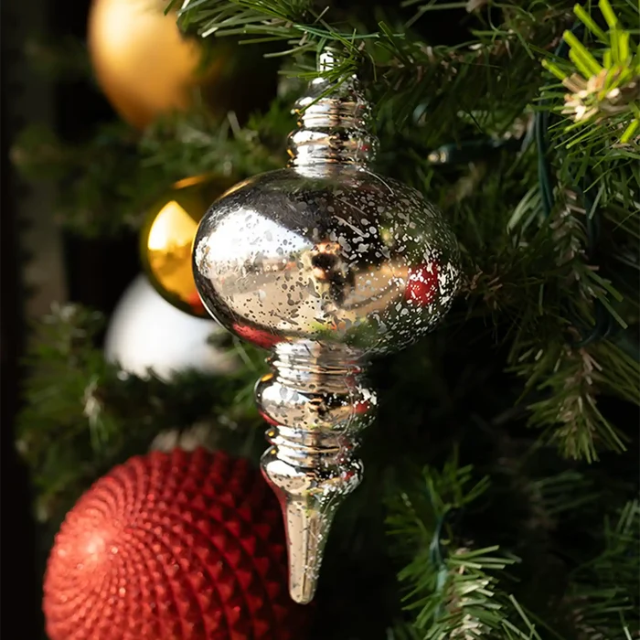 Silver mercury finial decorative Christmas ornament on a tree with gold and red balls in the background