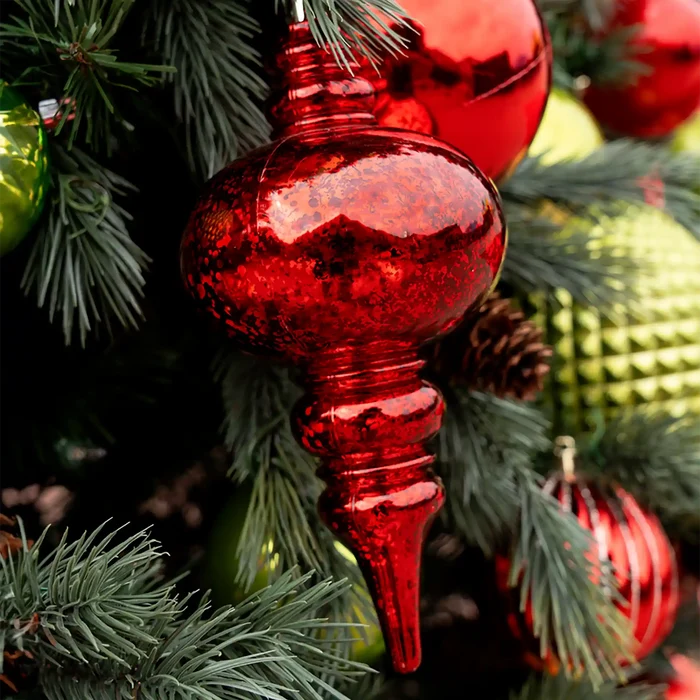 Red mercury ornament on a Christmas tree with green pine branches and other ornaments.