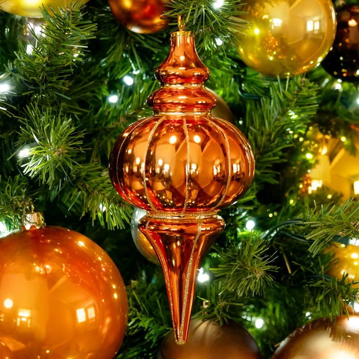 A metallic copper Christmas tree topper ornament hanging on a green Christmas tree with lights and other gold and copper ornaments.