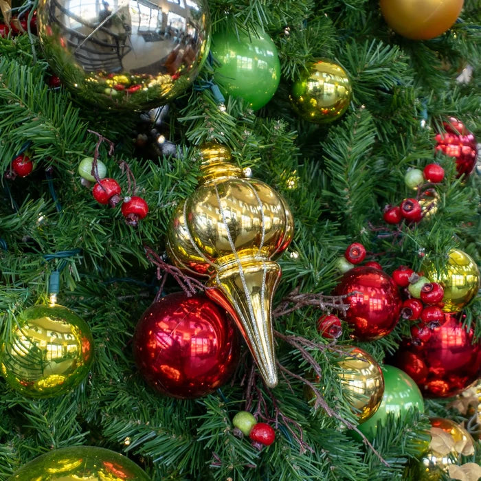 Close-up of a decorated Christmas tree with shiny red, gold, and green ornaments, red berries, and green pine needles.